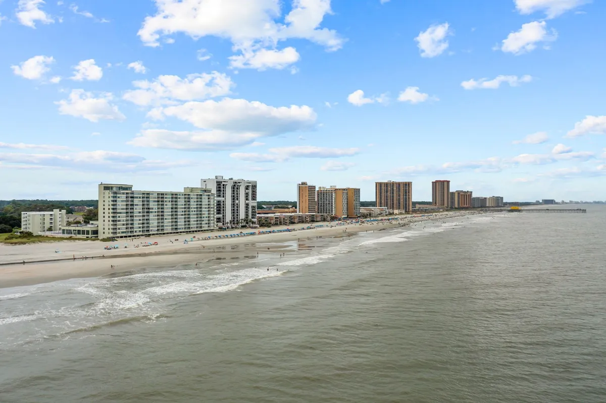This image presents a sweeping view of beachfront buildings with the ocean waves rolling in under a cloudy sky. The shoreline is inviting for walks, and the overall atmosphere is relaxed, hinting at the slower pace and natural beauty that winter guests can enjoy.