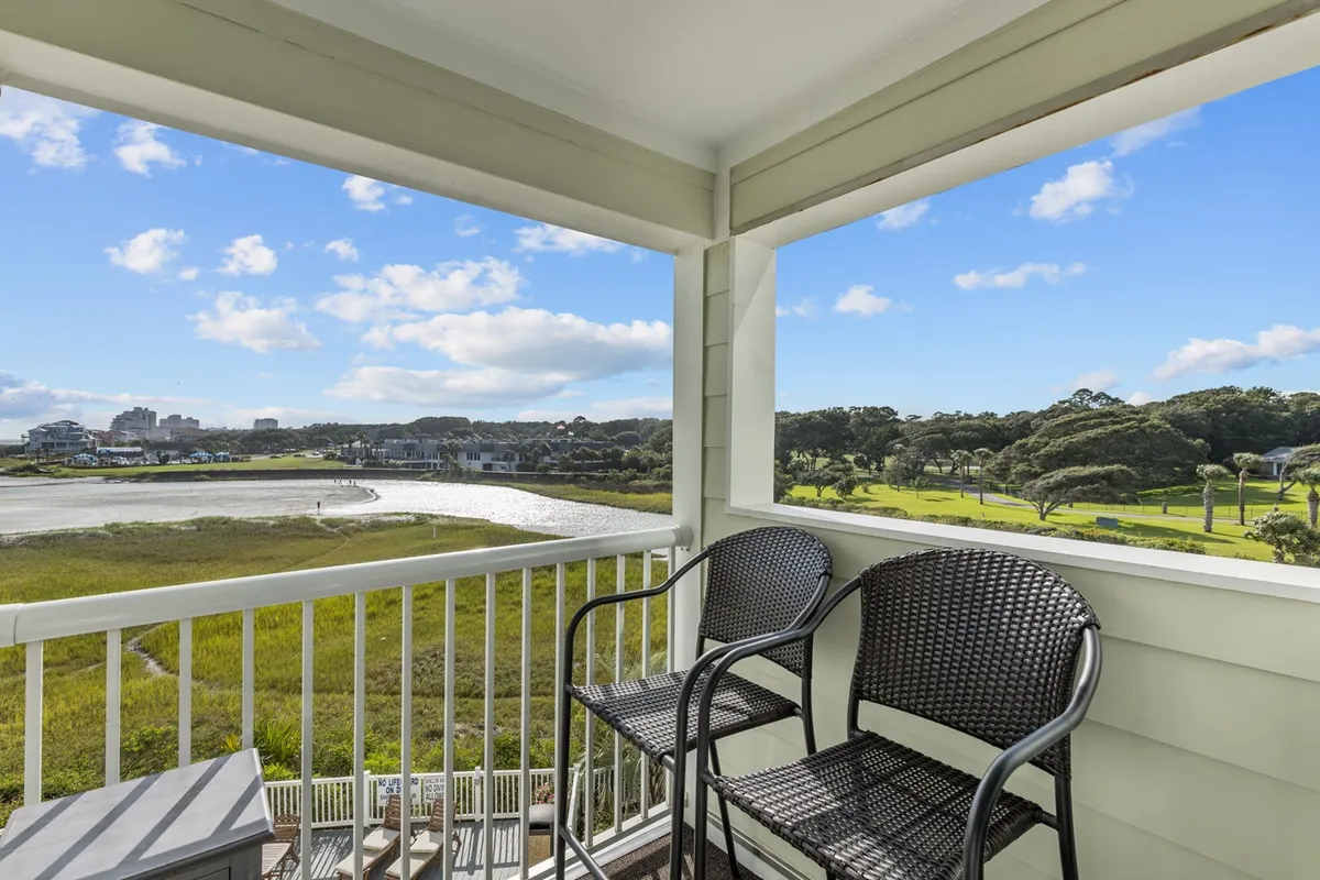 A private balcony with comfortable chairs overlooks a lush, green riverscape, offering a peaceful place to unwind while taking in the panoramic view. The scene is bathed in soft light and radiates quiet intimacy.