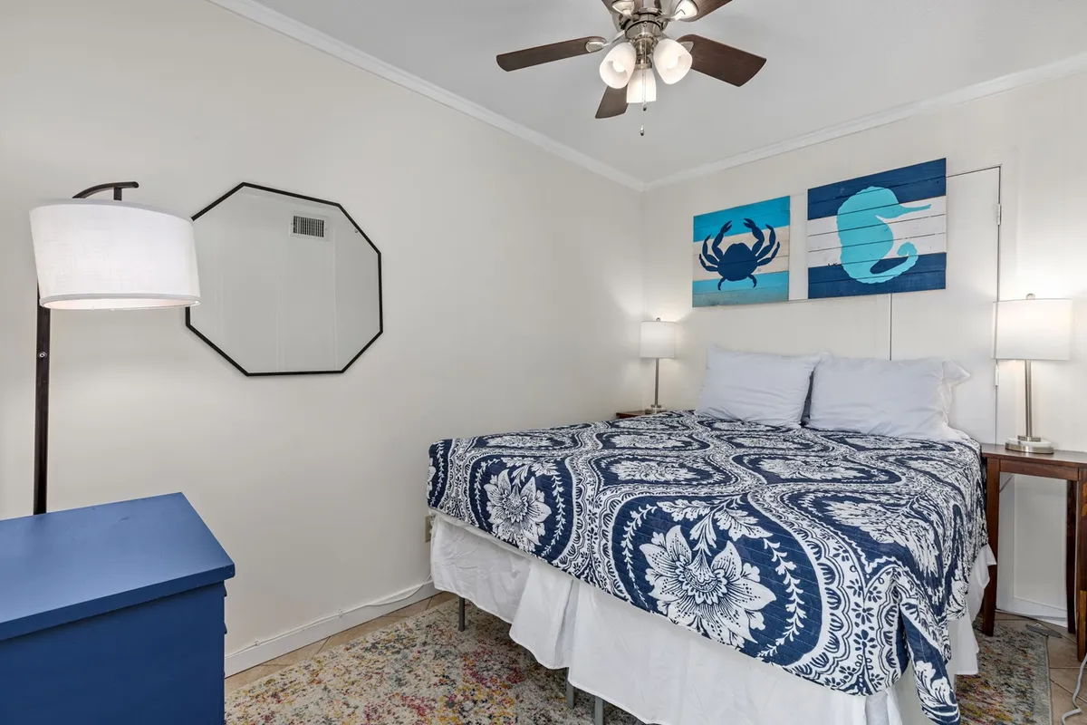 This image shows a beautifully decorated bedroom featuring a bed with blue and white patterned bedding, complemented by crab and seahorse artwork above the headboard and lamps on both bedside tables. Soft natural light fills the room, giving it a calm and tranquil atmosphere perfect for restful sleep.