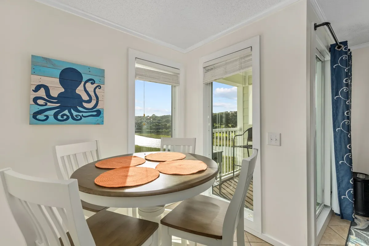 A round dining table sits beside large windows that frame a sweeping water view, accented by playful octopus wall art. The space is set for casual dining or relaxed gatherings with family and friends.