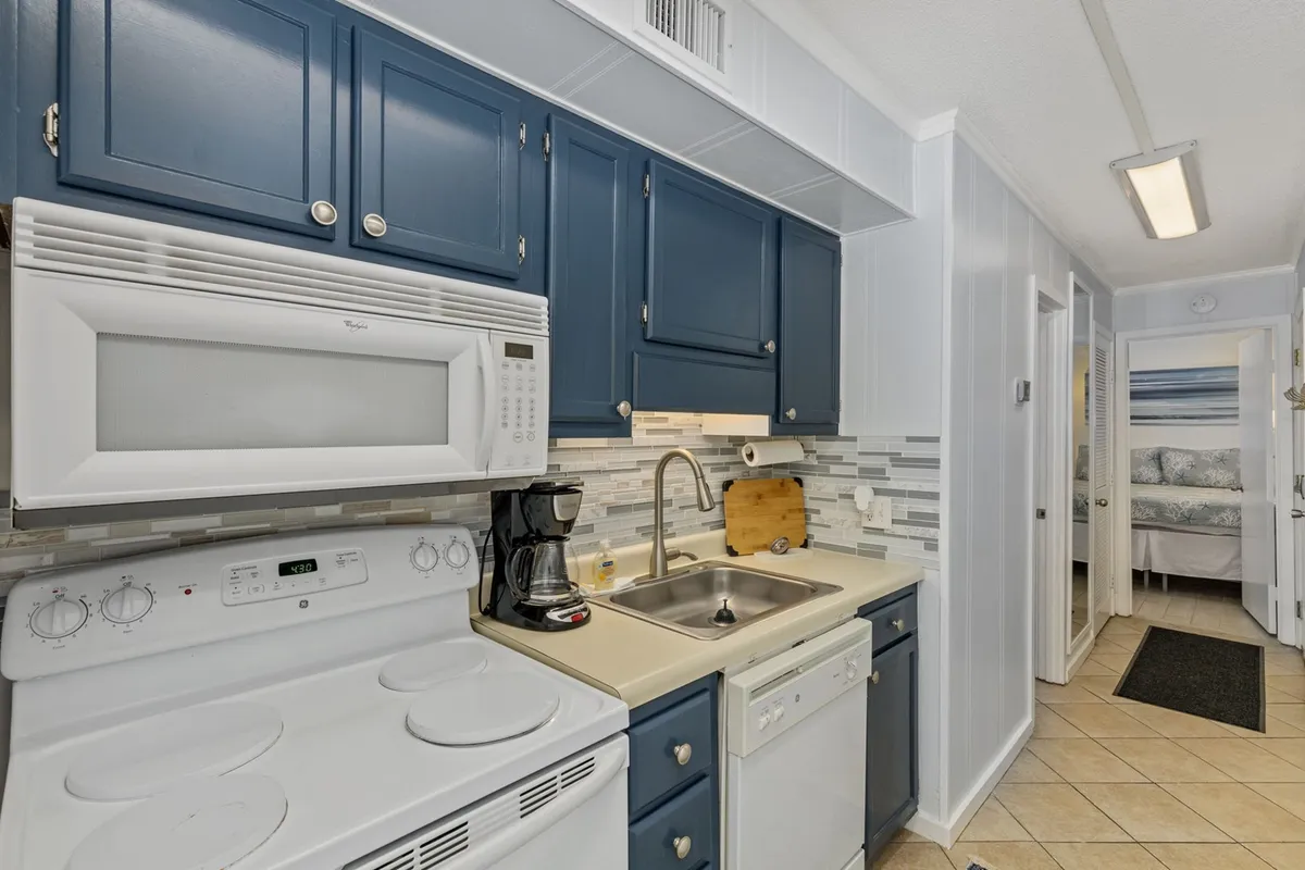 This image captures the heart of the kitchen featuring modern blue cabinets, a spacious countertop, stainless steel appliances, and a welcoming sink area. There are signs of activity with meal prep underway, evoking a sense of home-cooked gatherings and shared culinary experiences.